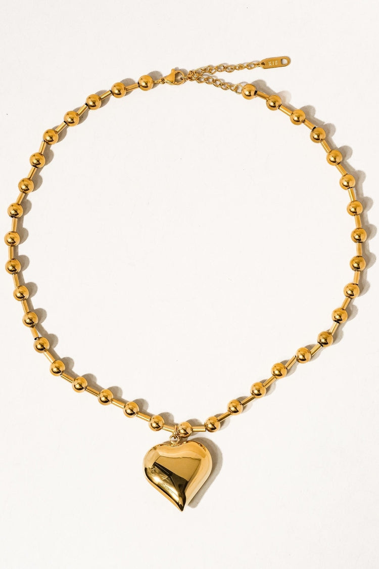 Gold necklace with a heart-shaped pendant on a white background