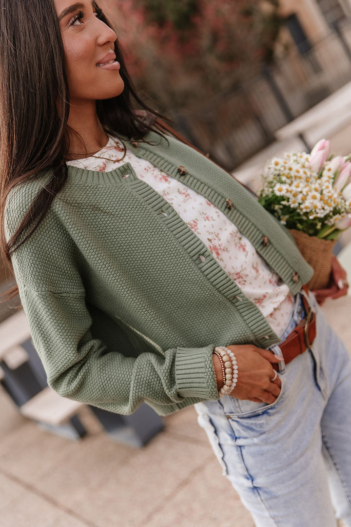 Woman wearing soft green cloud knit cardigan in fern color with relaxed fit layered over casual outfit