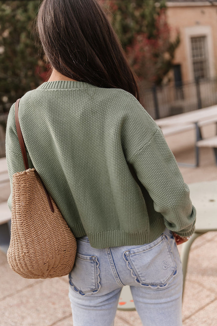 Woman wearing soft green cloud knit cardigan in fern color with relaxed fit layered over casual outfit