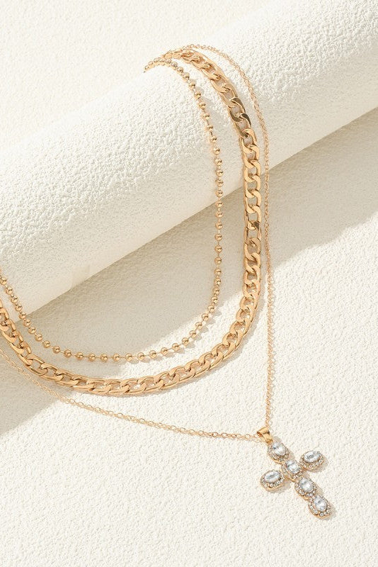 Gold chain necklace with a cross pendant on a textured white surface