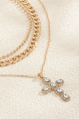 Gold chain necklaces with a cross pendant on a light beige surface