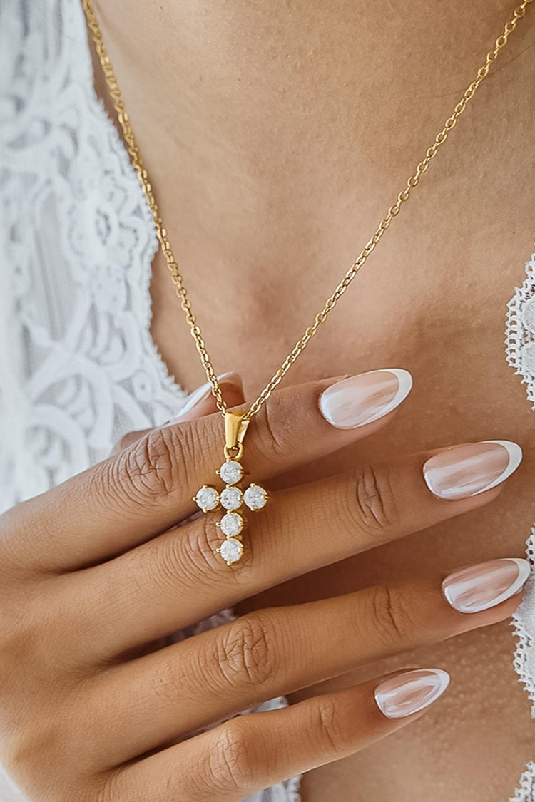 Gold necklace with a pendant held by a hand against a lace background