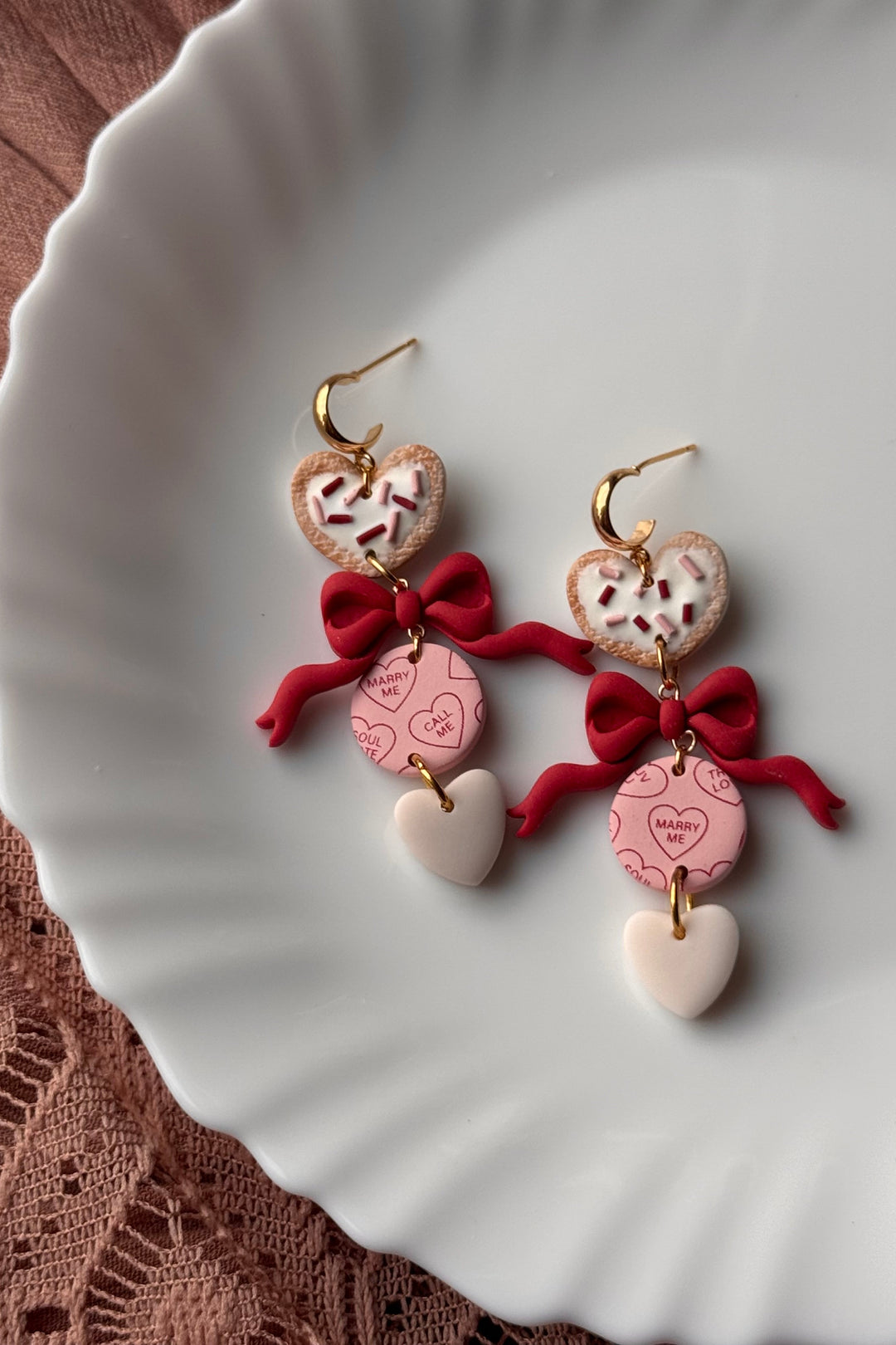 Heart-shaped earrings with red bows on a white dish
