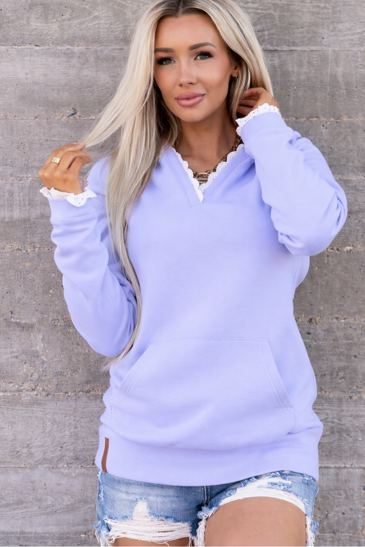 Woman wearing a light purple sweater with white trim against a gray concrete wall.