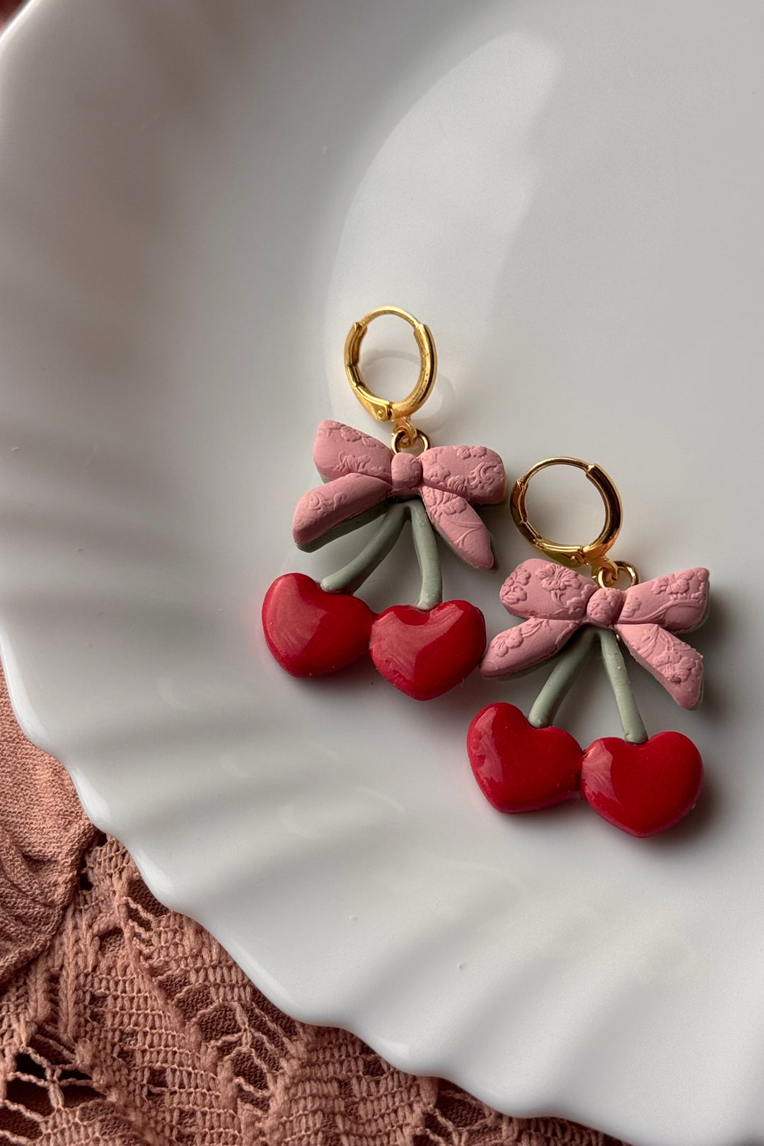 Pair of earrings with pink bows and red cherries on a white plate.
