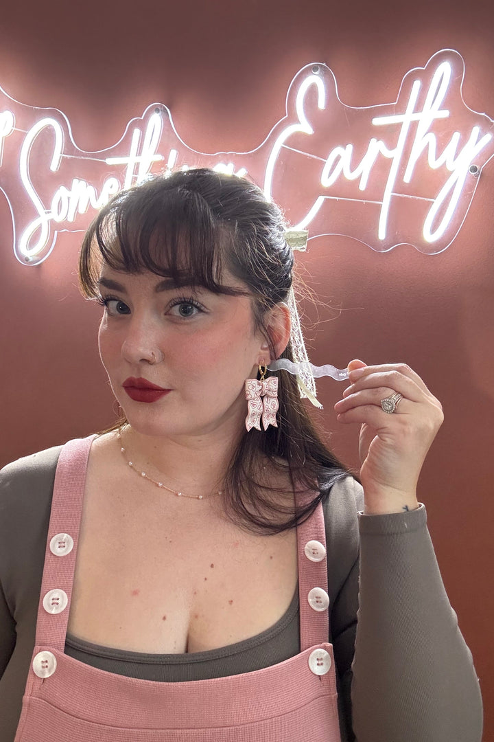 Woman holding a neon sign with 'Something Earthy' against a pink background