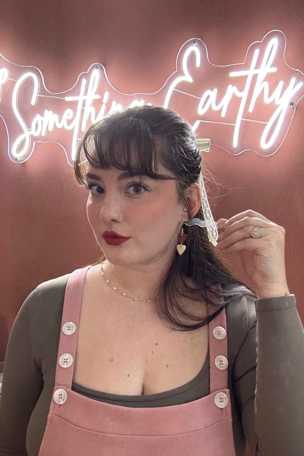 Woman adjusting her hair in front of a neon sign with 'Something Earthy' text.