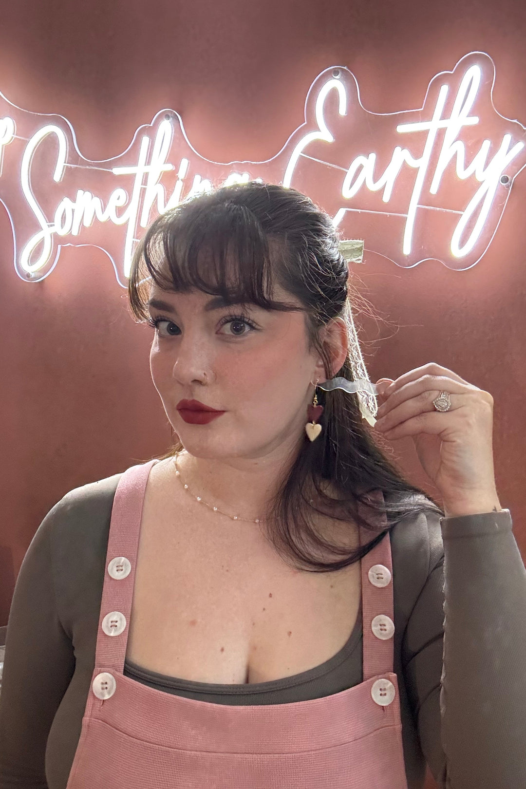 Woman adjusting her hair in front of a neon sign with 'Something Earthy' text.
