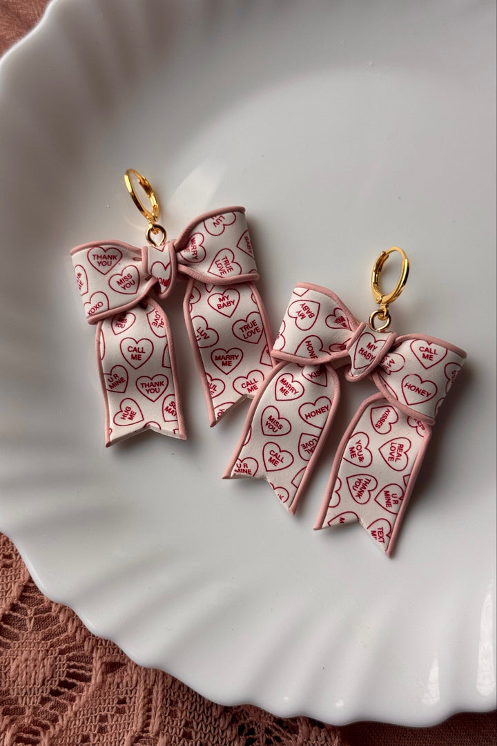 Pink bow-shaped earrings with heart patterns on a white plate.