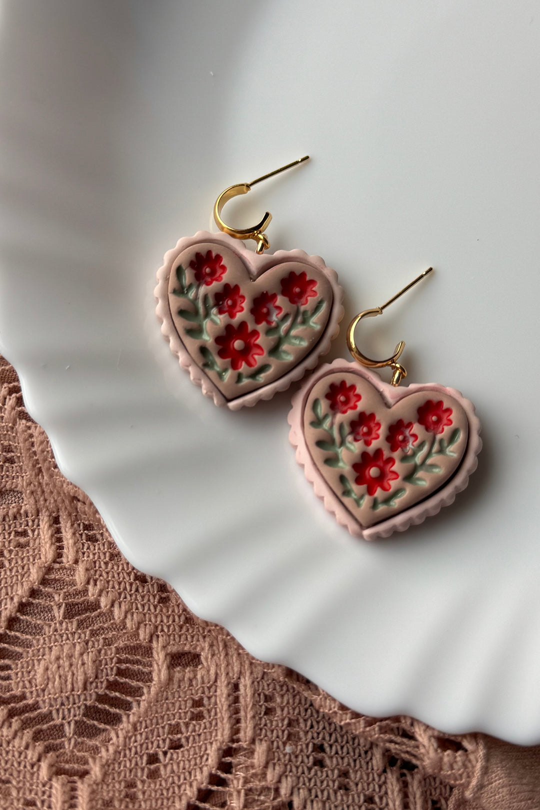 Heart-shaped earrings with floral design on a white plate with lace fabric.