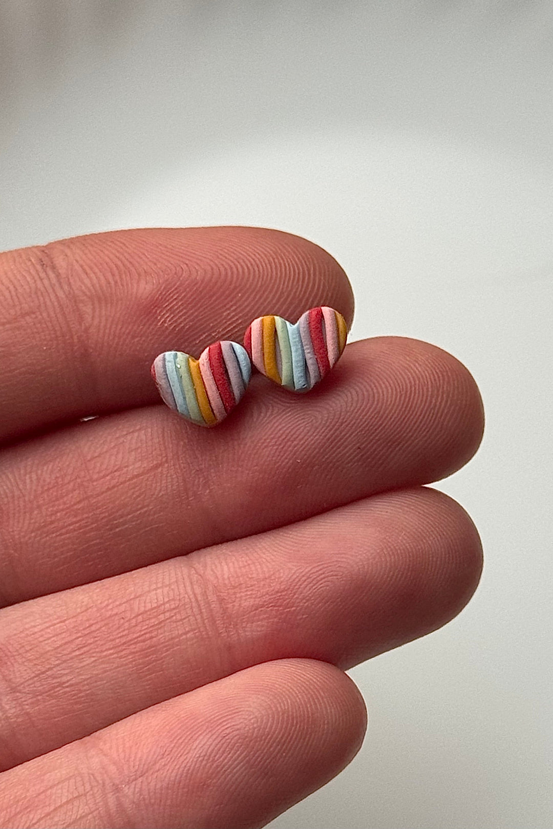 Colorful striped earrings held between fingers against a plain background