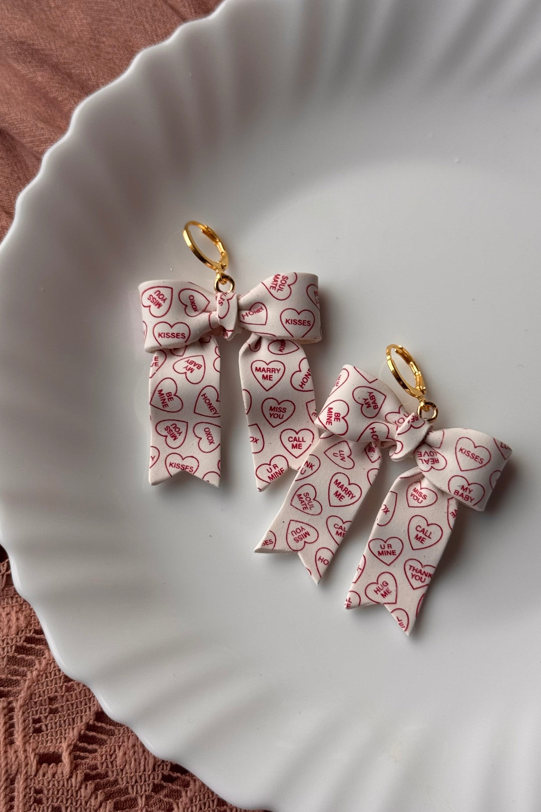 Bow-shaped earrings with heart patterns on a white plate