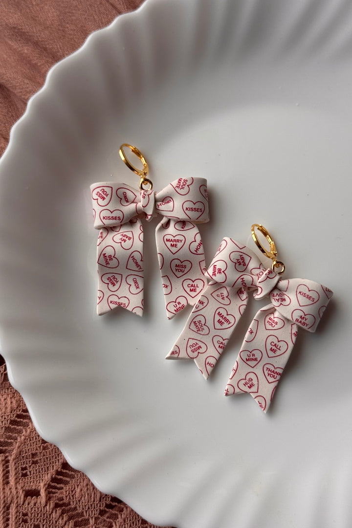 Bow-shaped earrings with heart patterns on a white plate