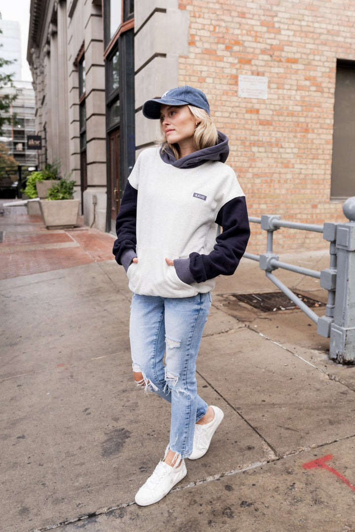 Person wearing a white and navy hoodie with blue jeans on a city street.