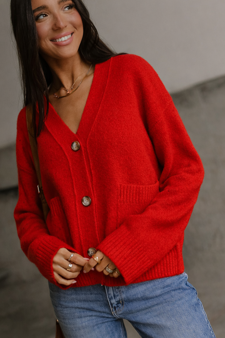 Woman wearing a red cardigan and blue jeans against a neutral background