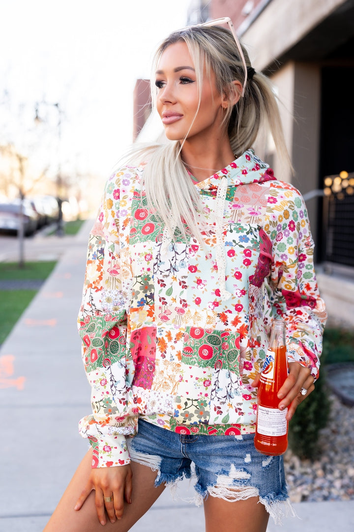 Woman wearing a colorful floral blouse and denim shorts, holding a bottle outdoors.