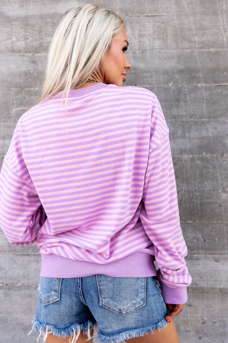 Woman wearing a pink and white striped sweater and denim shorts against a gray wall.