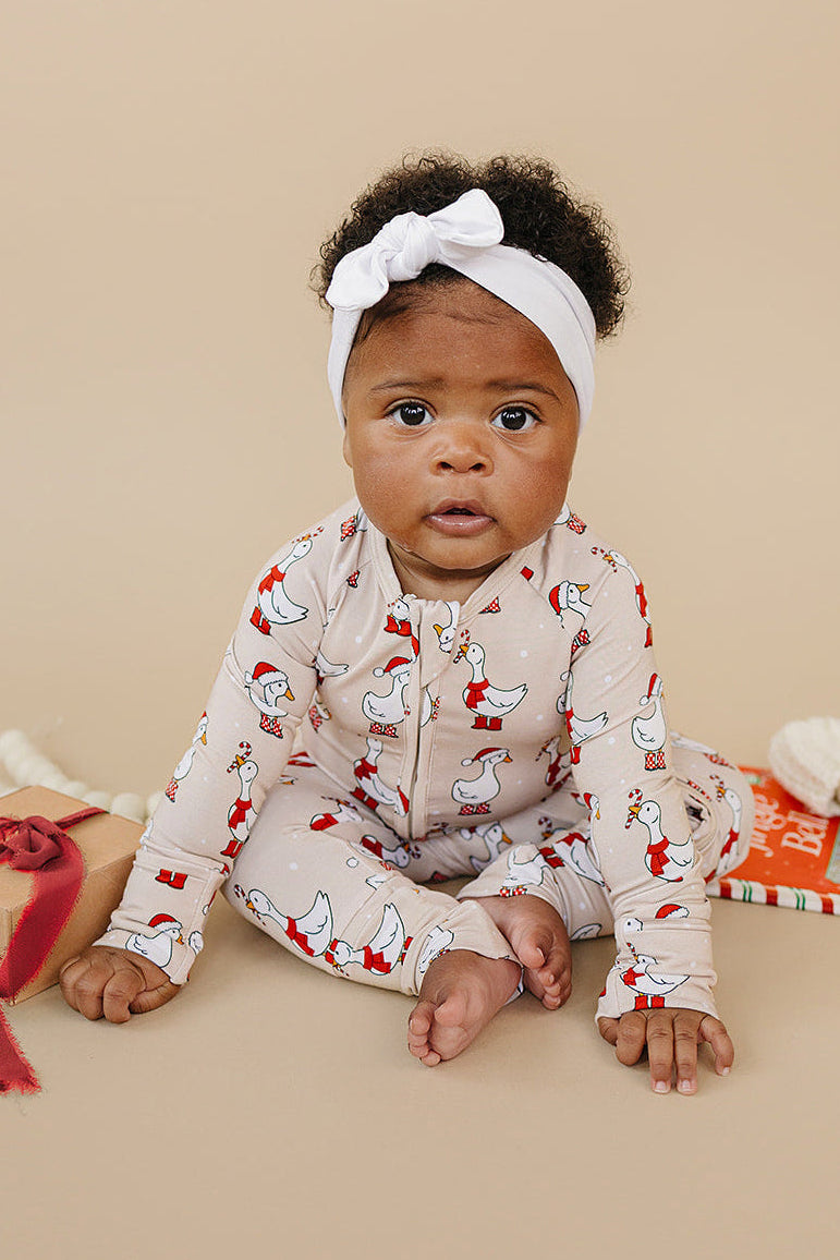 Baby wearing a patterned outfit with a white headband, sitting on a beige surface.