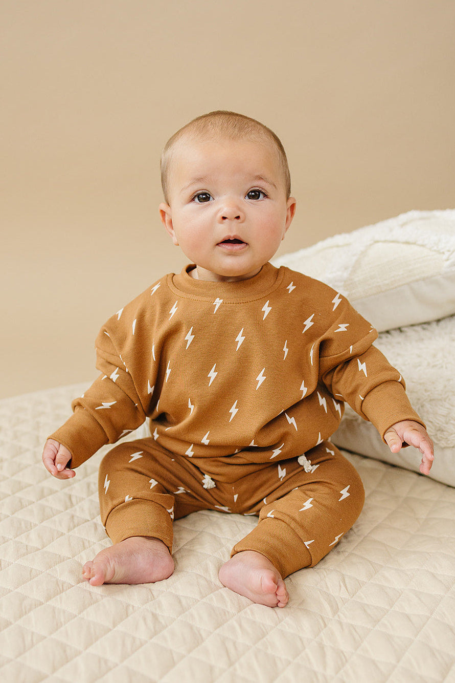 Baby wearing a brown outfit with white patterns on a beige blanket